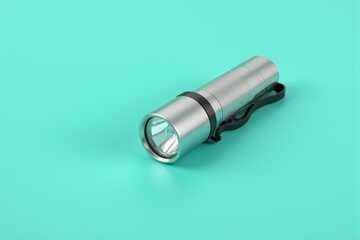 A compact flashlight with a metallic body on a pastel turquoise background