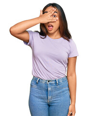 Young latin woman wearing casual clothes peeking in shock covering face and eyes with hand, looking through fingers with embarrassed expression.