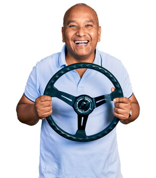 Hispanic middle age man holding steering wheel smiling and laughing hard out loud because funny crazy joke.