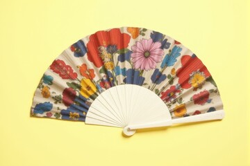 A designer hand fan with vibrant prints displayed on a pastel lemon background