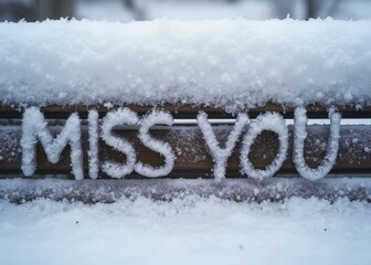 MISS YOU written in soft, icy letters across a snow covered bench, with snowflakes slowly collecting on its surface