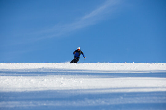 Skier descending a snowy slope under a vibrant blue sky in Kitzb&uuml;hel