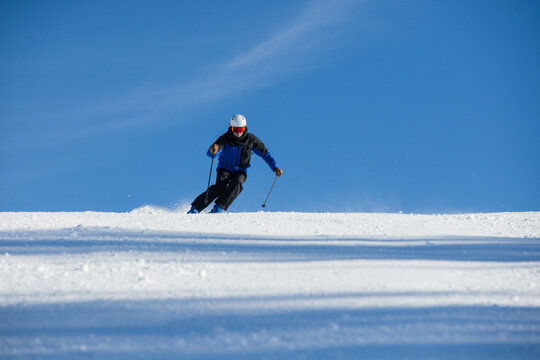 Skier descending a snowy slope under a vibrant blue sky in Kitzb&uuml;hel