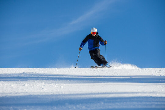 Skier descending a snowy slope under a vibrant blue sky in Kitzb&uuml;hel