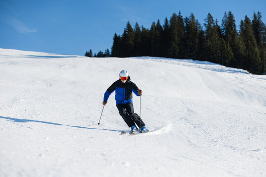 Skier carving on a snowy slope in Kitzb&uuml;hel under a bright blue sky
