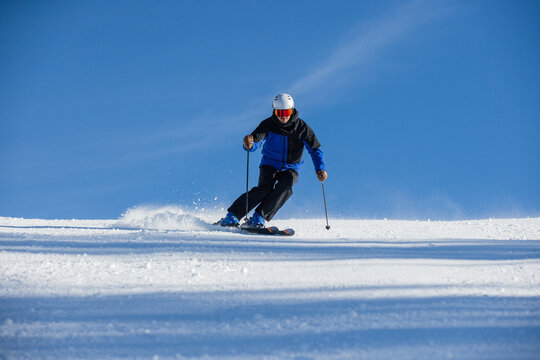 Skier descending a snowy slope under a vibrant blue sky in Kitzb&uuml;hel