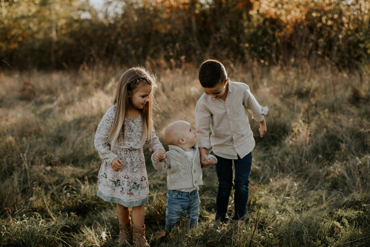 Cute interaction between three sweet siblings outdoors, grassy field