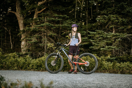 Female cyclist stands next to her mountain bike in the forest.