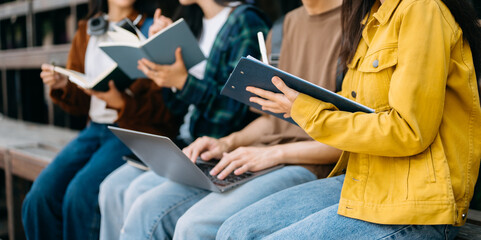 Young people college students is reading a book while relaxing sitting on grass in a campus park