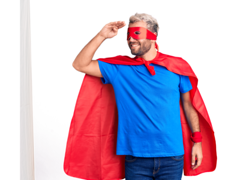Young blond man wearing super hero custome very happy and smiling looking far away with hand over head. searching concept.