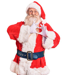 Old senior man with grey hair and long beard wearing traditional santa claus costume smiling in love doing heart symbol shape with hands. romantic concept.