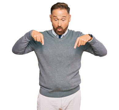 Handsome middle age man wearing business clothes pointing down with fingers showing advertisement, surprised face and open mouth