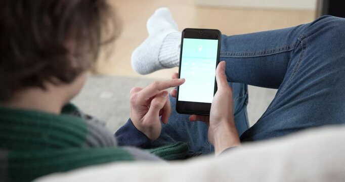 Relaxing at home, person using smartphone app for smart home control