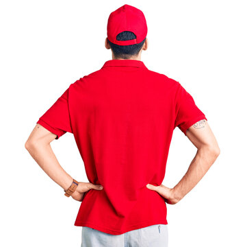 Young handsome man with beard wearing delivery uniform standing backwards looking away with arms on body