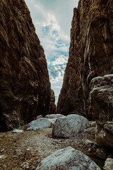 View from within a narrow gorge in Iran, looking out towards the cloudy sky. Large boulders and towering rock walls create a dramatic landscape. Photographed on November 12, 2024.