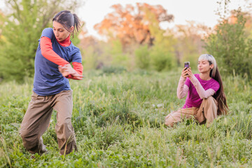 Two young women filming dancing performance in nature