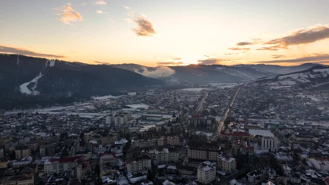 Drone footage of a snowy Gura Humorului cityscape, highlighting the scenic Partia Soimul slope and a stunning sunset
