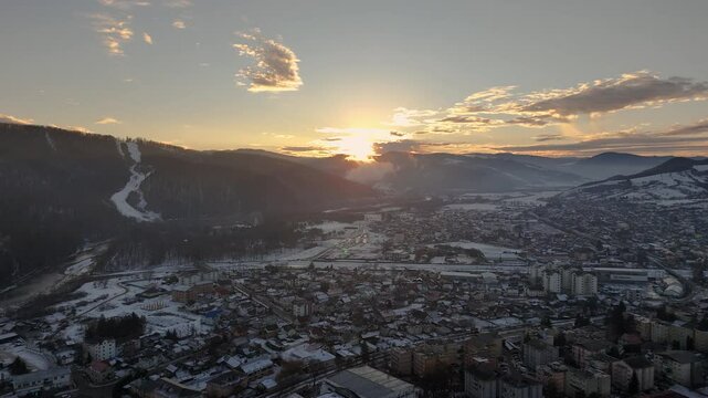 Aerial winter view of Gura Humorului, Romania, showcasing snow-covered buildings and the Partia Soimul ski slope at sunset
