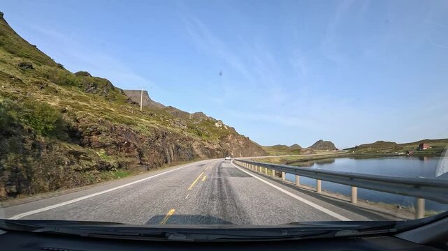 Driving through the tundra of northern Norway on E69 road. Rocky hills with grass surround the area, with a scenic lake visible on the right side.