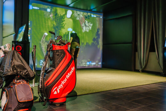 Close-up of a TaylorMade golf bag with clubs in an indoor Trackman simulator, featuring a virtual golf course displayed on the screen.