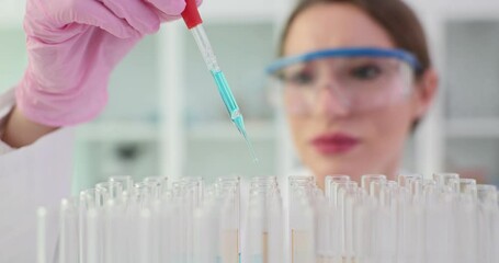 Woman laboratory worker pours liquid with pipette into test tubes on rack. Careful female technician prepares specimen for conducting experiment - Powered by Adobe