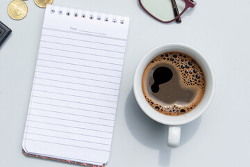 A blank note placed on the table alongside a cup of coffee and scattered coins, symbolizing financial planning, budgeting, and savings ideas.