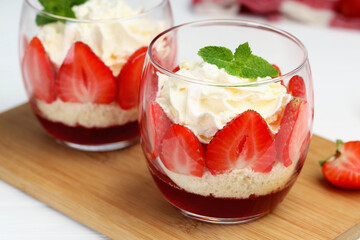 Tasty trifle dessert. Sponge cake, strawberries, jam and whipped cream in glasses on table, closeup