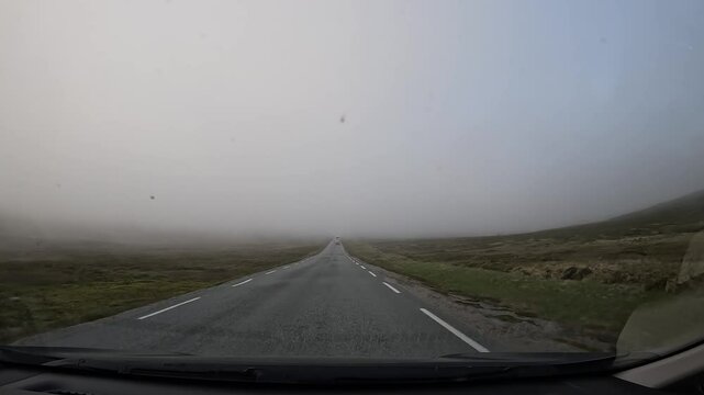 Driving through the tundra in northern Norway on E69 road. Surrounded by grassy landscapes under foggy conditions. The Arctic wilderness offers a serene and mysterious atmosphere.