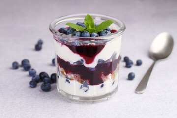 Tasty trifle dessert. Blueberries, sponge cake and whipped cream in glass on light grey table