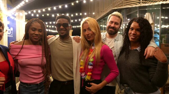Portrait of multi-ethnic friends standing at bar terrace at night