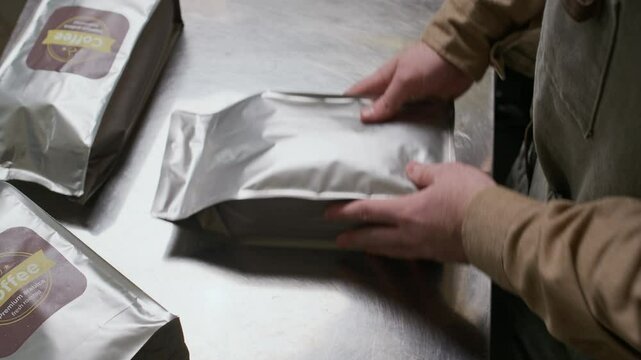 Close up of hands of unrecognizable worker sticking labels on bags with roasted coffee at factory