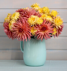 Bouquet of pink and yellow dahlias and chrysanthemums in a enameled light blue pitcher