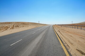 Winding black asphalt road through the sand dunes of  United Arab Emirates. An asphalt road zigzagging through the desert and sand dunes in the United Arab Emirates