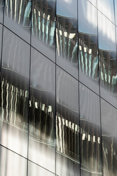 This image captures a modern building's reflective glass facade, showcasing abstract patterns created by the interplay of light and reflections from nearby structures.