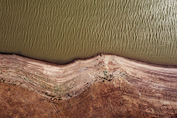 drone view of river with rippled water surface flowing near stony shore with dried surface in...