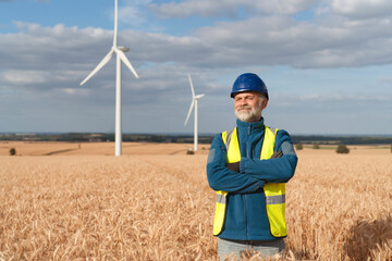 Renewable energy worker stands confidently in a wheat field with wind turbines against a cloudy sky