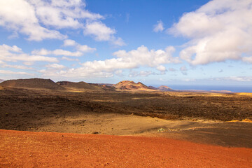 Extensive red sandy plains in the middle of the desert with blue sky and clouds