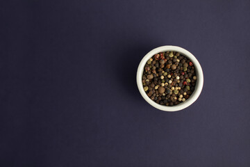 Top view of a bowl full of mixed peppercorns on a blue background