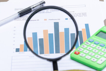 Obraz premium Magnifying Glass Zooming in on Financial Bar Chart with Calculator and Pen for Data Analysis Concept