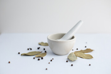 White mortar with black pepper and bay leaves on a white background.