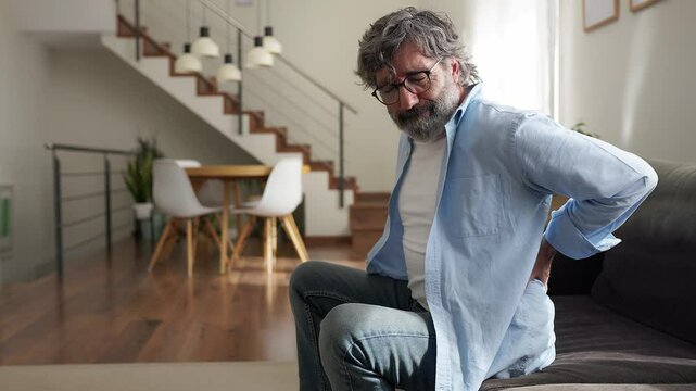 Senior man suffering from back pain while sitting on sofa