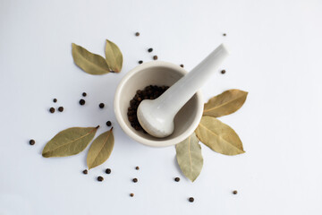 White mortar with black pepper and bay leaves on a white background.