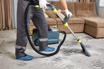A professional worker in safety gear meticulously cleans a carpet using a powerful vacuum cleaner....