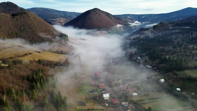 Aerial View of a Mountain Village in the Carpathians, Morning Fog Covers Houses, Fields, and Forests in the Valley