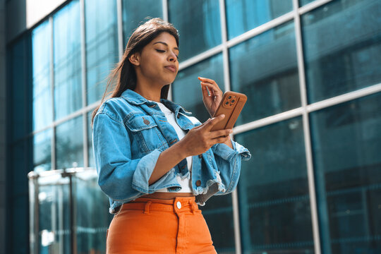 Young woman using smartphone in front of modern glass building during bright day - Powered by Adobe