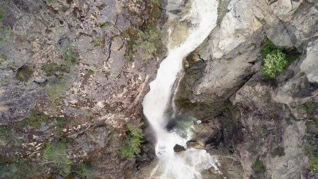 Two tier waterfall cascades down steep rustic rock canyon, aerial view