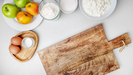 Wooden cutting board with baking ingredients, green and red apples, flour, eggs, sugar, perfect for homemade apple pie recipes