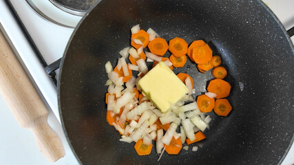 Diced onions, carrots, and a chunk of butter sizzle in a pan, embodying homestyle cooking and comfort food preparation