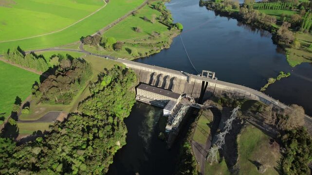 Aerial drone shot of hydroelectric dam and reservoir, surrounded by greenery and rural landscapes.