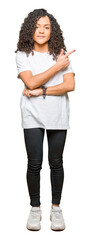 Obraz premium Young beautiful woman with curly hair wearing white t-shirt Pointing with hand finger to the side showing advertisement, serious and calm face